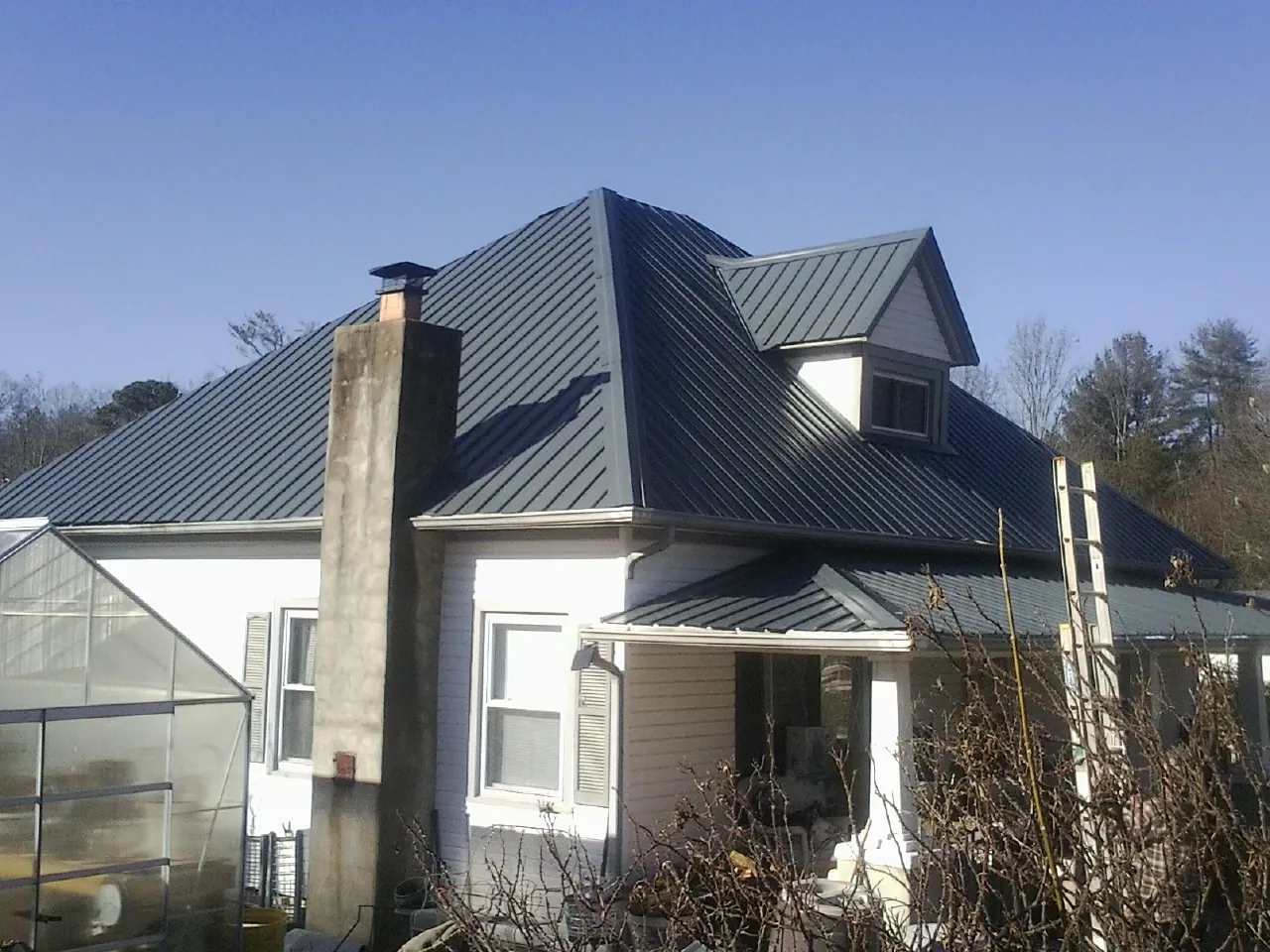 Dark blue standing seam metal roof on a white farmhouse with dormer — Slate & Tile Roof Repair by Roofing Brothers in Admire