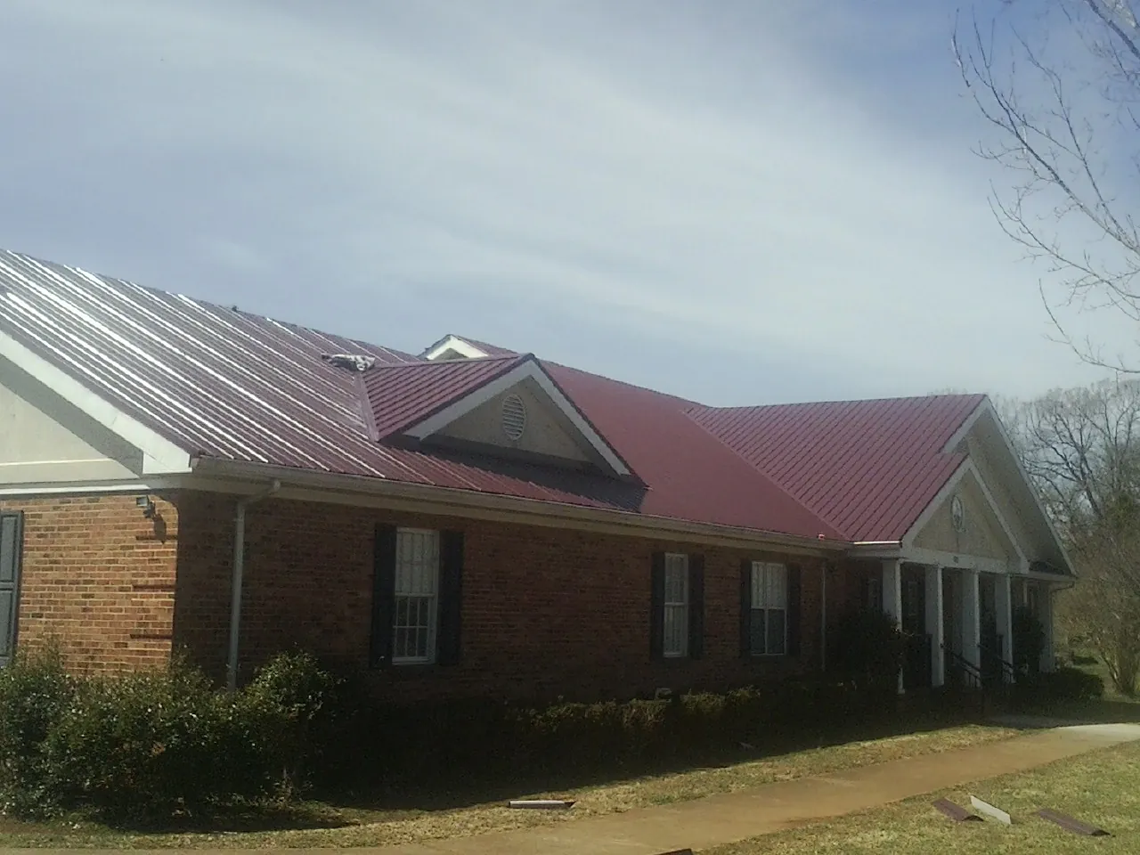 Red metal roof with gabled entries on a long brick building, from a Hail Damage Roof Repair job in Admire