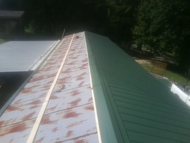Old rusted panels beside newly installed green metal roofing — Wind Damage Roof Repair by Roofing Brothers in Admire