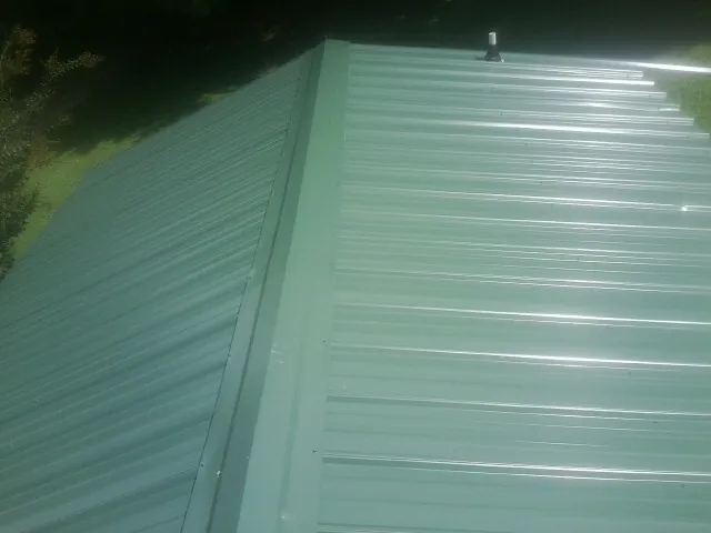 New green metal panels meeting at the ridge of a roof — Flat Roof Repair work by our crew in Admire