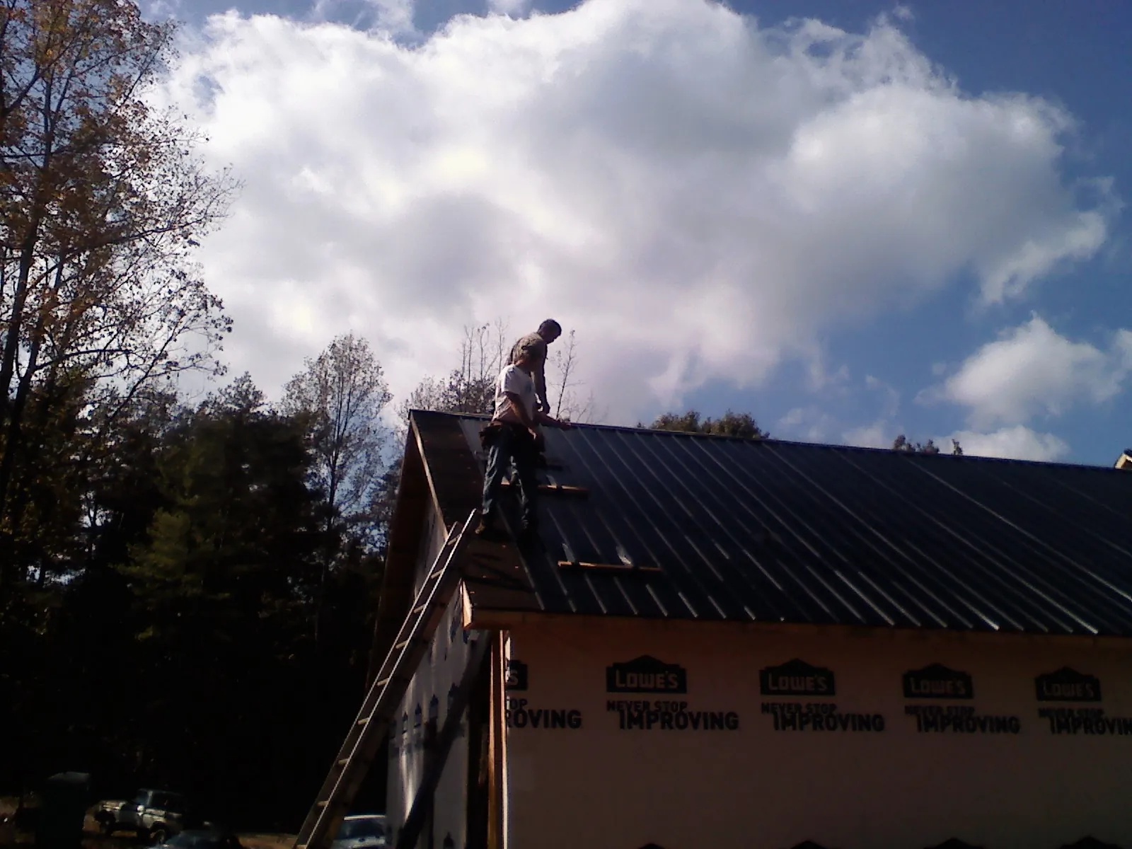 Roofer fastening dark metal panels high against a cloudy sky, from a Roof Inspection job in Admire