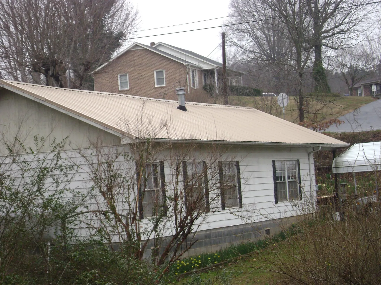 Tan metal roof on a white sided house set into a hillside — Commercial Roofing by Roofing Brothers in Admire